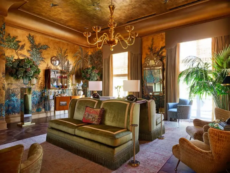 Luxurious living room showcasing 2026 interior design color trends with golden tropical murals, velvet sofas, and chandelier.